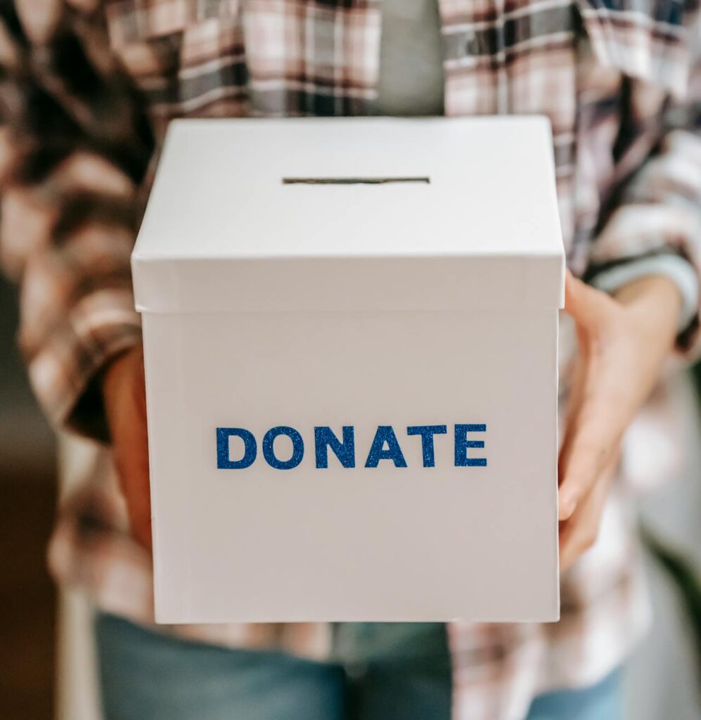 Cropped photo of an anonymous person holding a white box with the word 'Donate' on it in blue letters.